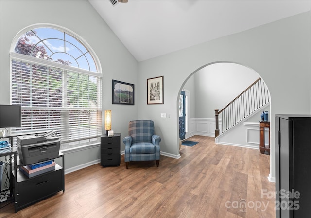 sitting room featuring arched walkways, wood finished floors, stairway, and high vaulted ceiling