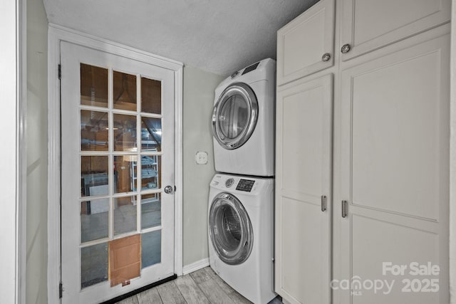 3905 NC Highway 213, Marshall, NC 28753 - washroom featuring stacked washing machine and dryer, cabinet space, light wood-type flooring, a textured ceiling, and baseboards