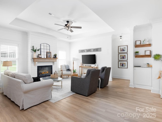 living area featuring a tray ceiling, light wood-style flooring, a ceiling fan, and ornamental molding