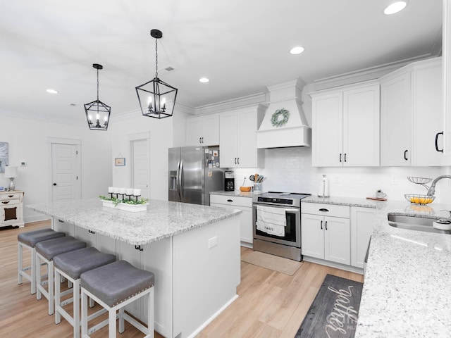 kitchen with stainless steel appliances, a sink, premium range hood, a kitchen island, and white cabinetry
