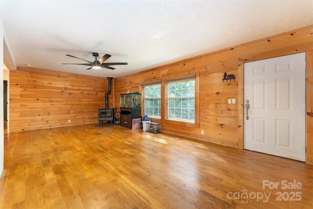 116 Hidden Meadow Dr Unit 17, Candler, NC 28715 - unfurnished living room with a wood stove, wood walls, ceiling fan, and light wood-type flooring