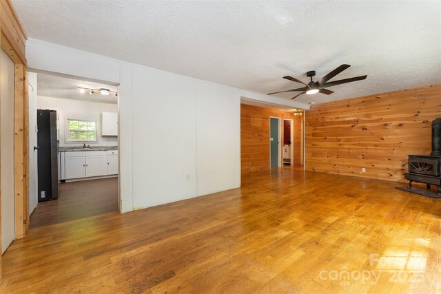 116 Hidden Meadow Dr Unit 17, Candler, NC 28715 - unfurnished living room with a wood stove, ceiling fan, light wood-type flooring, wood walls, and a textured ceiling