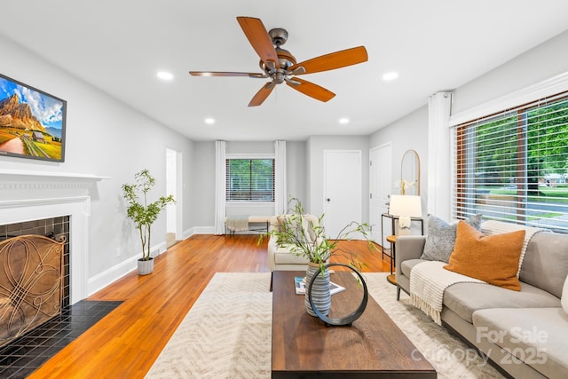living area featuring a ceiling fan, wood finished floors, recessed lighting, baseboards, and a tile fireplace