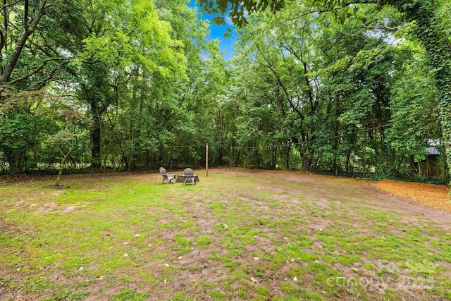 view of green lawn with a view of trees and a fire pit