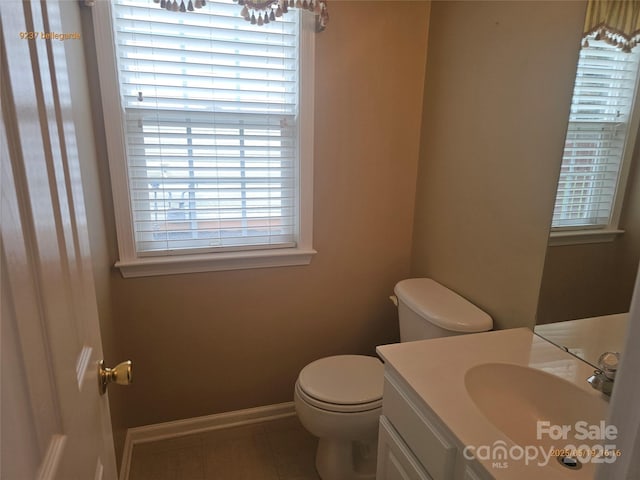 half bath featuring toilet, vanity, tile patterned floors, and baseboards
