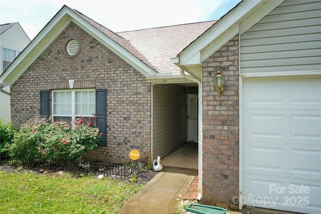entrance to property with brick siding, a shingled roof, and a garage