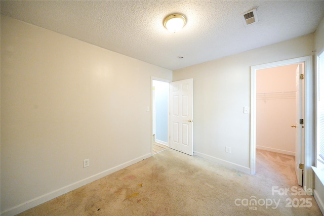 unfurnished bedroom with a walk in closet, carpet floors, baseboards, a closet, and a textured ceiling