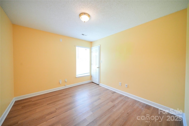 empty room with light wood-type flooring, baseboards, and a textured ceiling