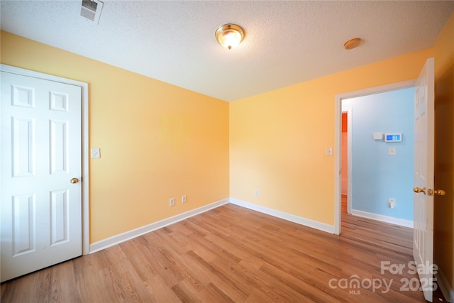 empty room with wood finished floors, a textured ceiling, a smoke detector, and baseboards