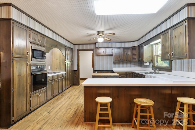 kitchen with oven, stainless steel microwave, a sink, a peninsula, and light wood finished floors