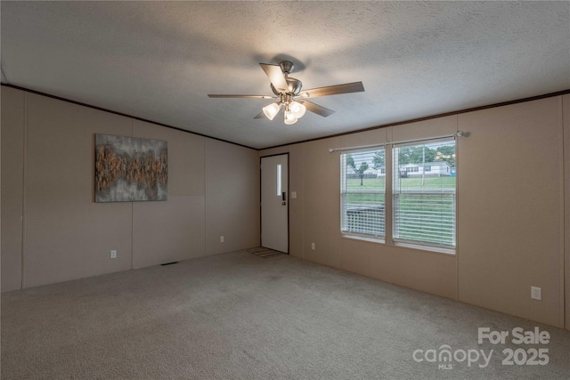 carpeted spare room with a ceiling fan, a textured ceiling, crown molding, and a decorative wall