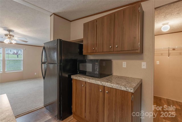 kitchen with black appliances, a textured ceiling, light wood-style floors, a ceiling fan, and brown cabinets