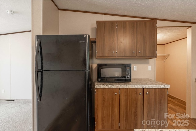 kitchen featuring black appliances, brown cabinetry, a textured ceiling, light countertops, and vaulted ceiling