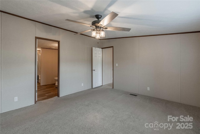 unfurnished bedroom with carpet, ornamental molding, connected bathroom, and ceiling fan