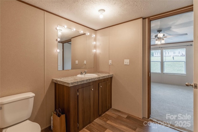 half bathroom with crown molding, toilet, vanity, wood finished floors, and ceiling fan