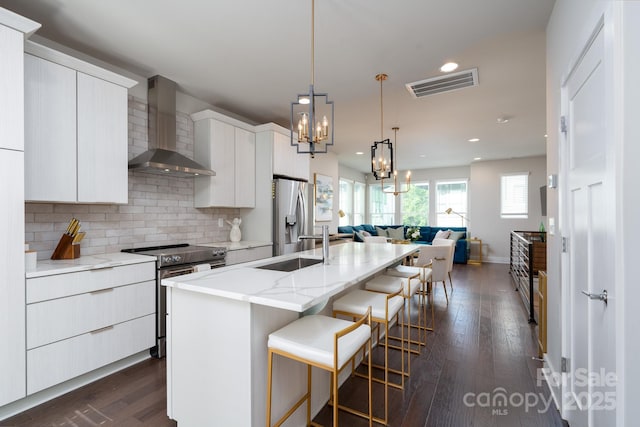 kitchen featuring wall chimney exhaust hood, appliances with stainless steel finishes, open floor plan, a breakfast bar, and a sink