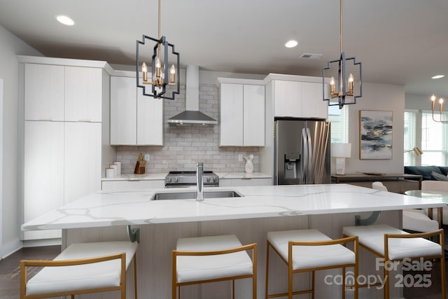 kitchen with stainless steel fridge, a chandelier, wall chimney range hood, a sink, and recessed lighting