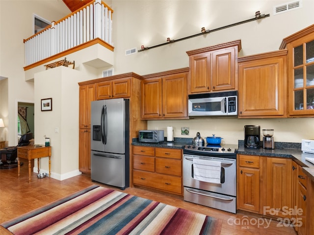 572 Multiflora Way, Waynesville, NC 28785 - kitchen featuring appliances with stainless steel finishes, a high ceiling, light wood-style floors, brown cabinetry, and glass insert cabinets