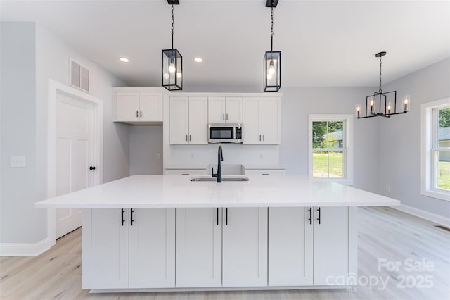 309 Walker St, Kannapolis, NC 28081 - kitchen featuring stainless steel microwave, white cabinetry, a spacious island, light wood finished floors, and light countertops