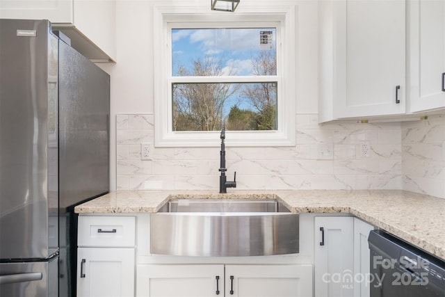 kitchen featuring freestanding refrigerator, dishwashing machine, a sink, white cabinetry, and backsplash