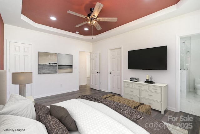 bedroom with a raised ceiling, recessed lighting, baseboards, dark wood finished floors, and ensuite bath