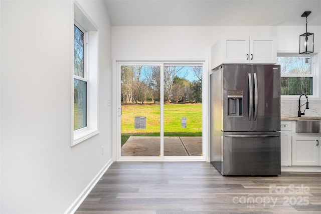 kitchen featuring stainless steel fridge, white cabinets, wood finished floors, light stone countertops, and hanging light fixtures