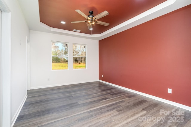 empty room with a raised ceiling, a ceiling fan, wood finished floors, recessed lighting, and baseboards