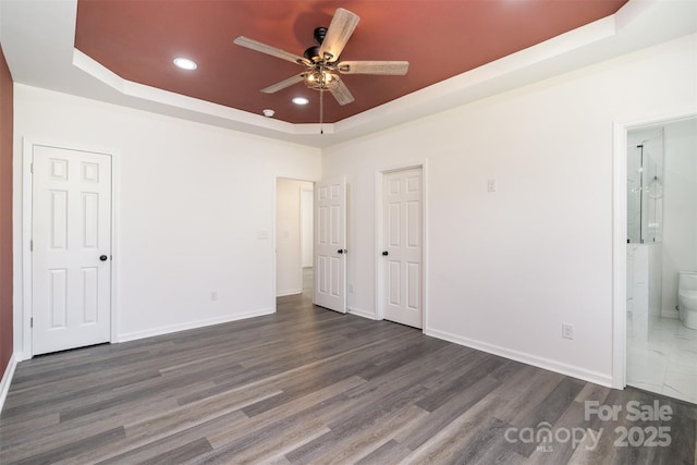 unfurnished bedroom with a raised ceiling, recessed lighting, dark wood-style flooring, baseboards, and connected bathroom