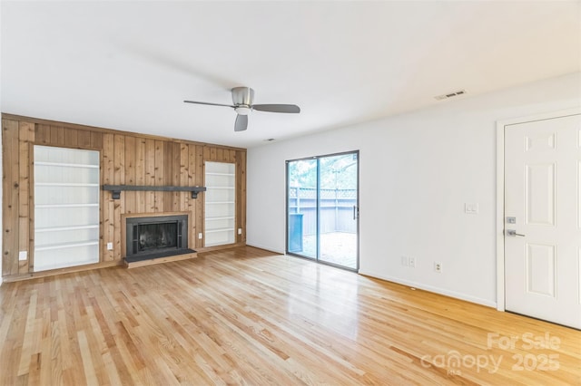 unfurnished living room featuring ceiling fan, wood walls, light wood-type flooring, a fireplace with raised hearth, and baseboards