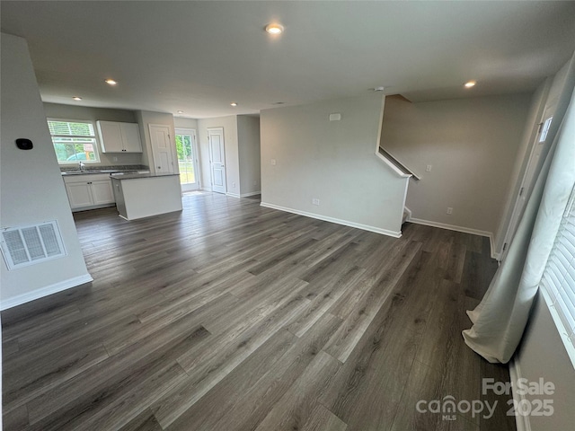 unfurnished living room featuring recessed lighting, a sink, baseboards, and dark wood-style floors