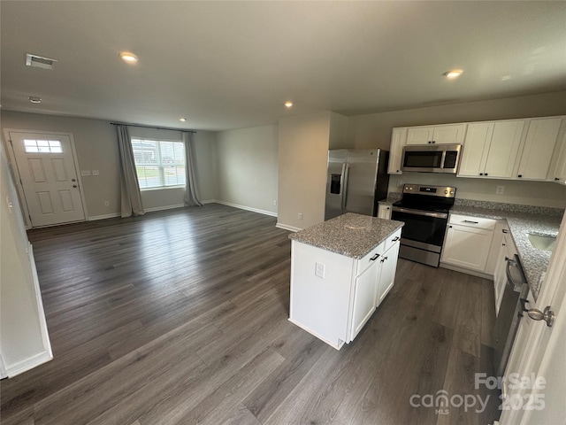 kitchen featuring stainless steel appliances, a center island, baseboards, light stone counters, and open floor plan