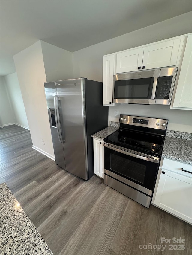 kitchen featuring stainless steel appliances, dark wood finished floors, light stone counters, and white cabinets