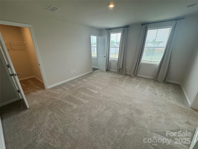 unfurnished bedroom with baseboards, light carpet, and a spacious closet