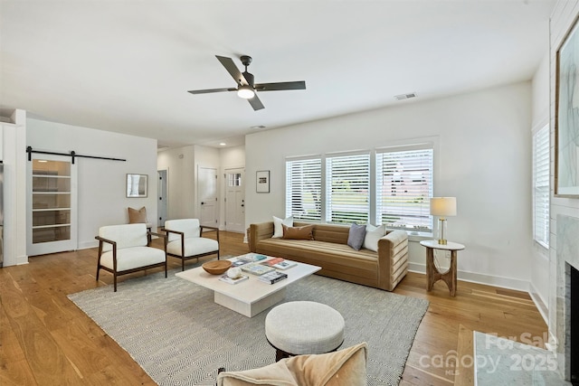 3163 Maury St, Charlotte, NC 28208 - living room with a barn door, light wood-style flooring, ceiling fan, a fireplace with flush hearth, and baseboards