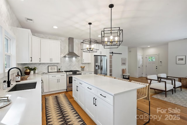 3163 Maury St, Charlotte, NC 28208 - kitchen with appliances with stainless steel finishes, wall chimney range hood, a sink, light wood finished floors, and a barn door