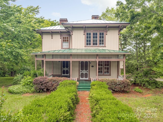 italianate house with a standing seam roof, a chimney, metal roof, and a porch
