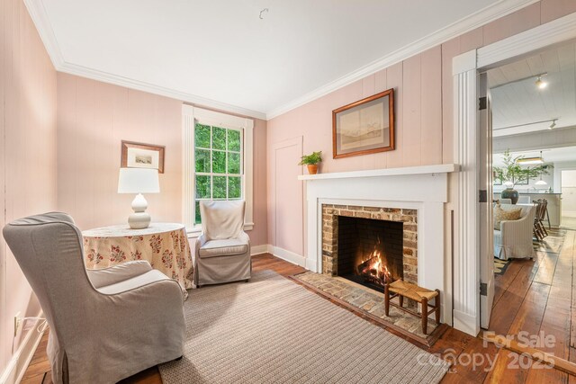 living area featuring wood finished floors, a fireplace, crown molding, and baseboards