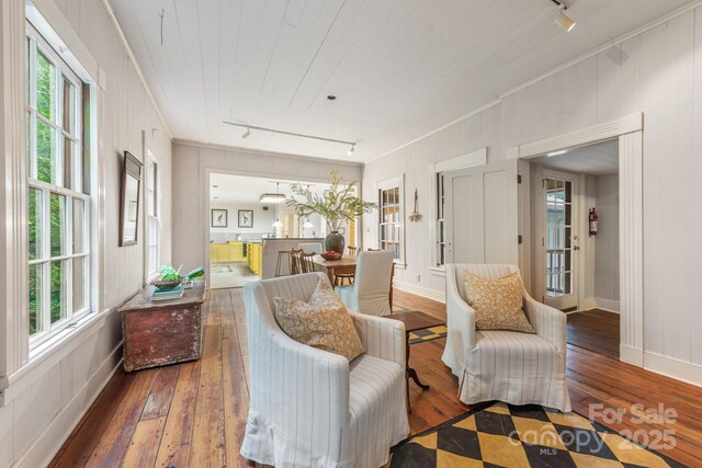 living area featuring track lighting, wood-type flooring, baseboards, and ornamental molding