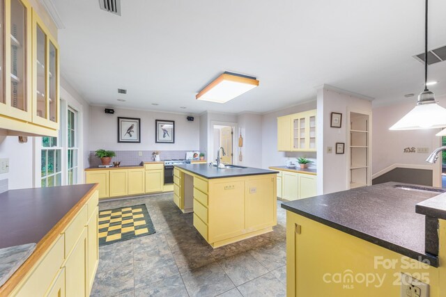 kitchen featuring a sink, dark countertops, a kitchen island with sink, glass insert cabinets, and crown molding