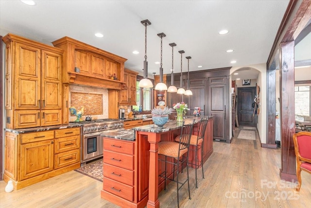 2461 Eagles Nest Rd, Waynesville, NC 28786 - kitchen with double oven range, arched walkways, light wood-type flooring, a center island, and a breakfast bar area