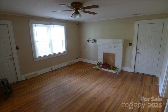 unfurnished living room with wood finished floors, ornamental molding, ceiling fan, baseboards, and a brick fireplace