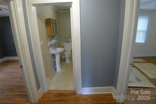 half bath with crown molding, baseboards, toilet, and wood finished floors