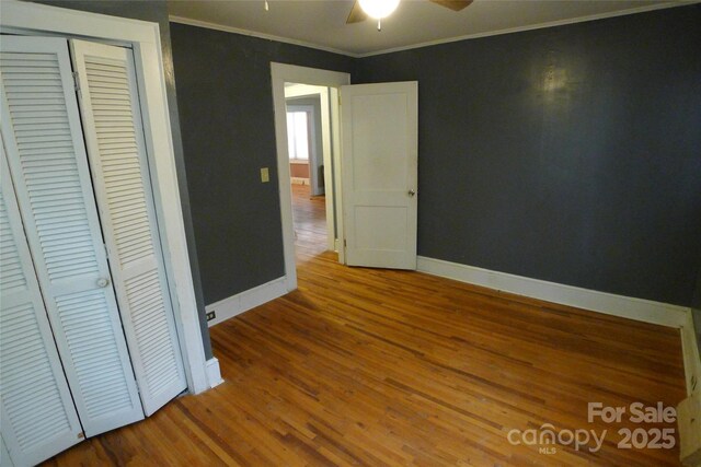 unfurnished bedroom with ornamental molding, baseboards, wood finished floors, a closet, and a ceiling fan