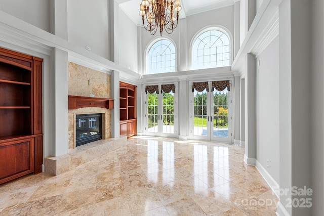 unfurnished living room with a high ceiling, french doors, crown molding, a chandelier, and a high end fireplace