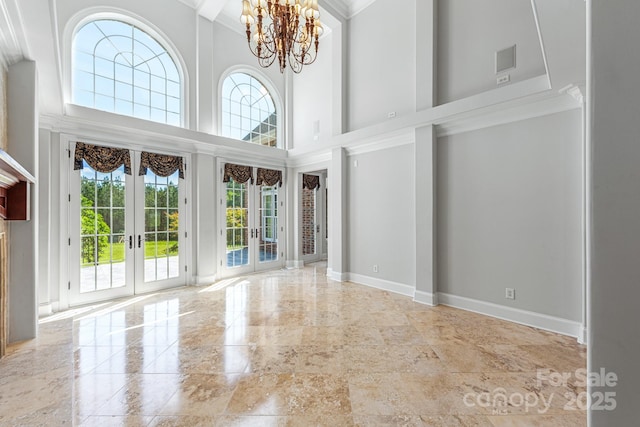 unfurnished room with french doors, healthy amount of natural light, ornamental molding, a chandelier, and a towering ceiling