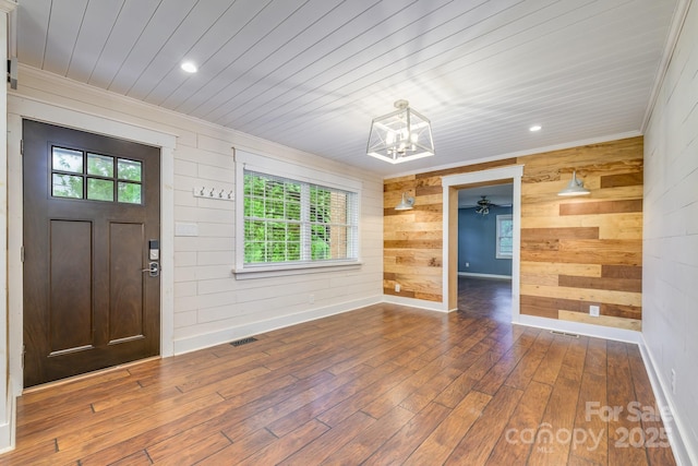 entrance foyer featuring wooden walls, ornamental molding, a chandelier, wood-type flooring, and baseboards