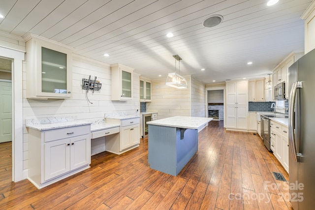 kitchen with appliances with stainless steel finishes, a kitchen island, dark wood finished floors, decorative backsplash, and a fireplace
