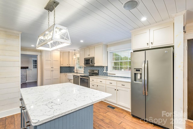 kitchen featuring appliances with stainless steel finishes, light wood finished floors, a kitchen island, light stone countertops, and recessed lighting