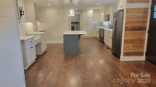 kitchen with appliances with stainless steel finishes, white cabinets, dark wood-type flooring, light countertops, and a kitchen island