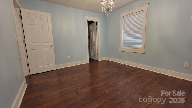 unfurnished room featuring dark wood-style flooring, baseboards, and a chandelier